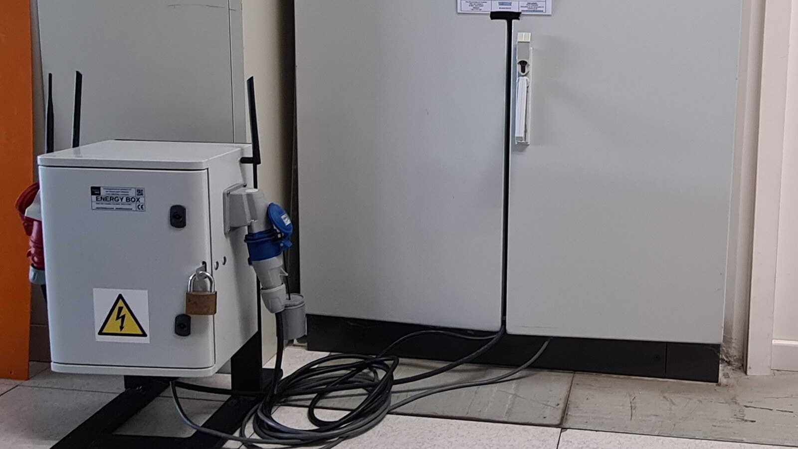 Coffret Energy-Box cadenassé, antennes déployées, câble d'alimentation industriel enroulé au sol devant une armoire électrique fermée