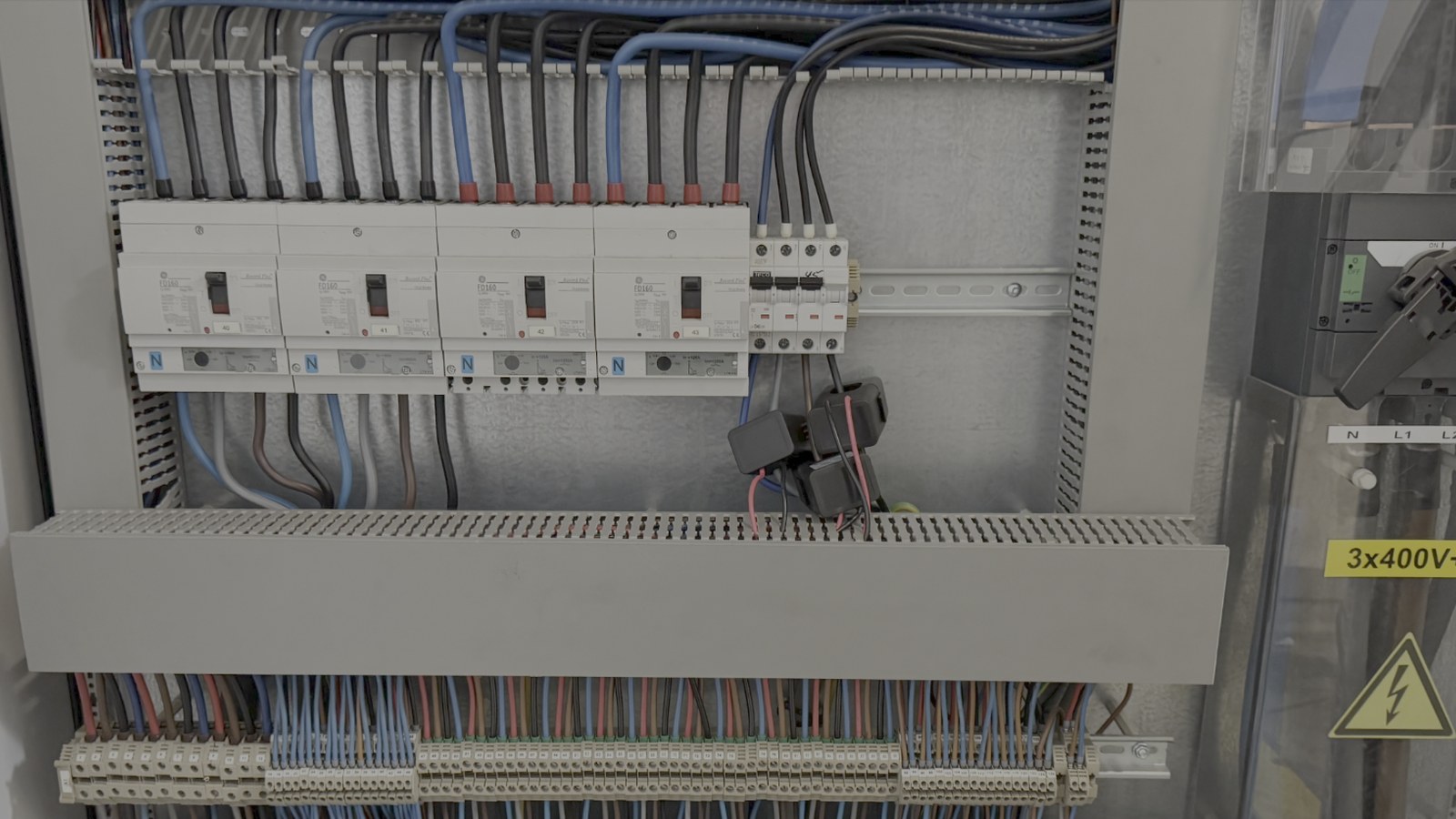 Armoire électrique ouverte, rangée de disjoncteurs et pinces ampérométriques installées sur les départs pour la mesure du courant