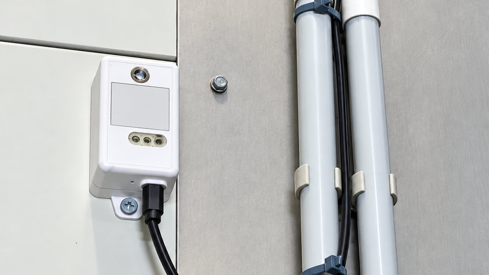Sonde de température LoRaWAN fixée sur la façade d'un équipement frigorifique, avec son câble de sonde déportée longeant deux tuyauteries