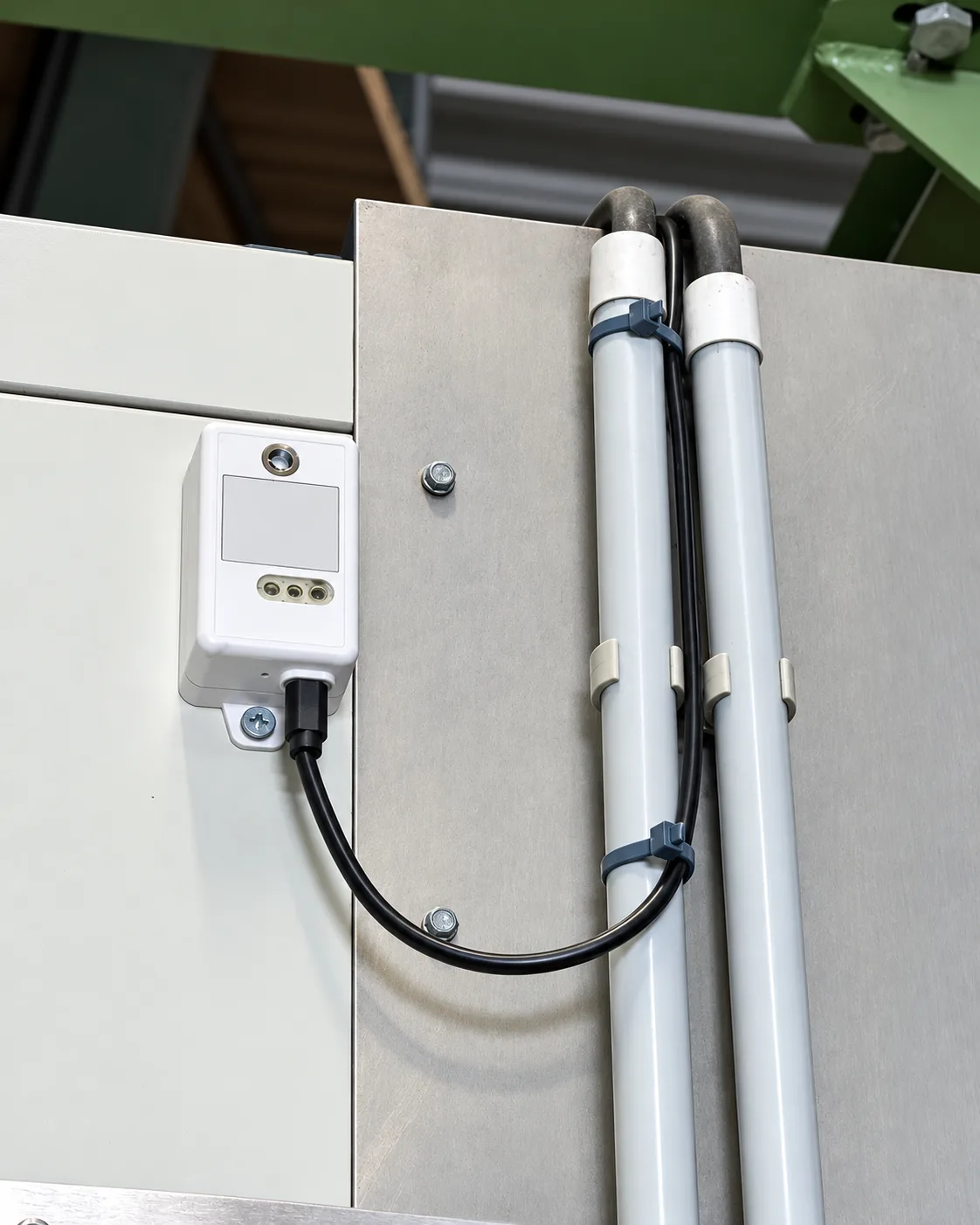 Sonde de température fixée sur la façade d'un équipement frigorifique, son câble noir longeant deux tuyauteries maintenues par des colliers