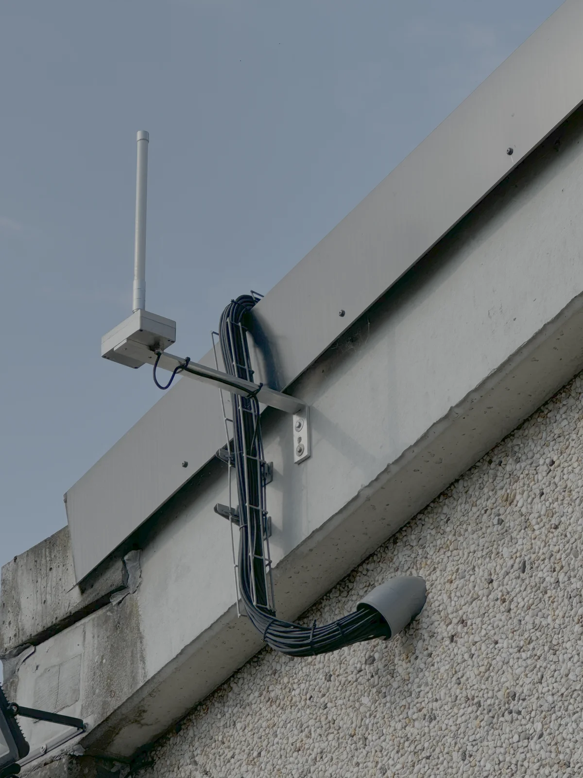 Antenne en fibre de verre montee sur un support depasse d'un pignon de batiment, cable descendant dans un chemin de cables.
