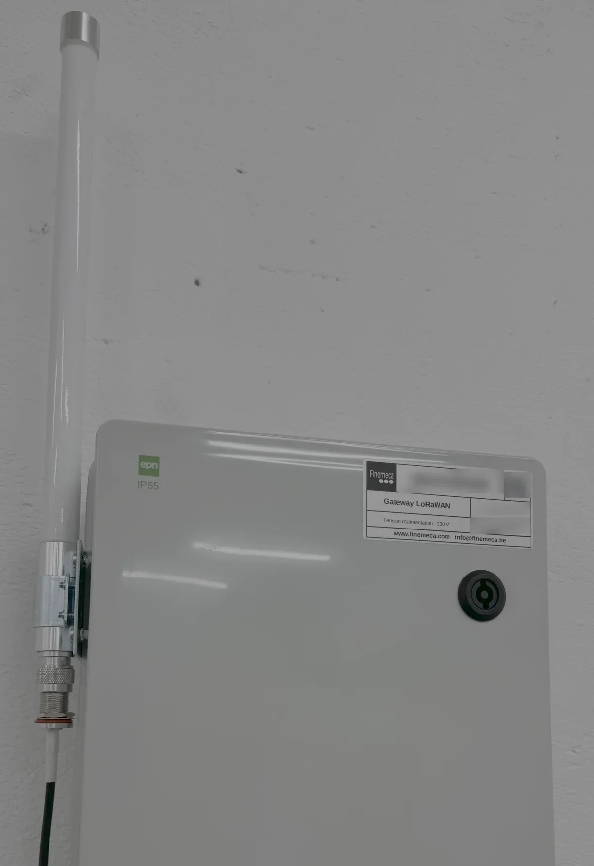 Antenne en fibre de verre fixee sur le flanc d'un boitier synthetique IP65 abritant une gateway LoRaWAN, raccordee par un connecteur traversant.