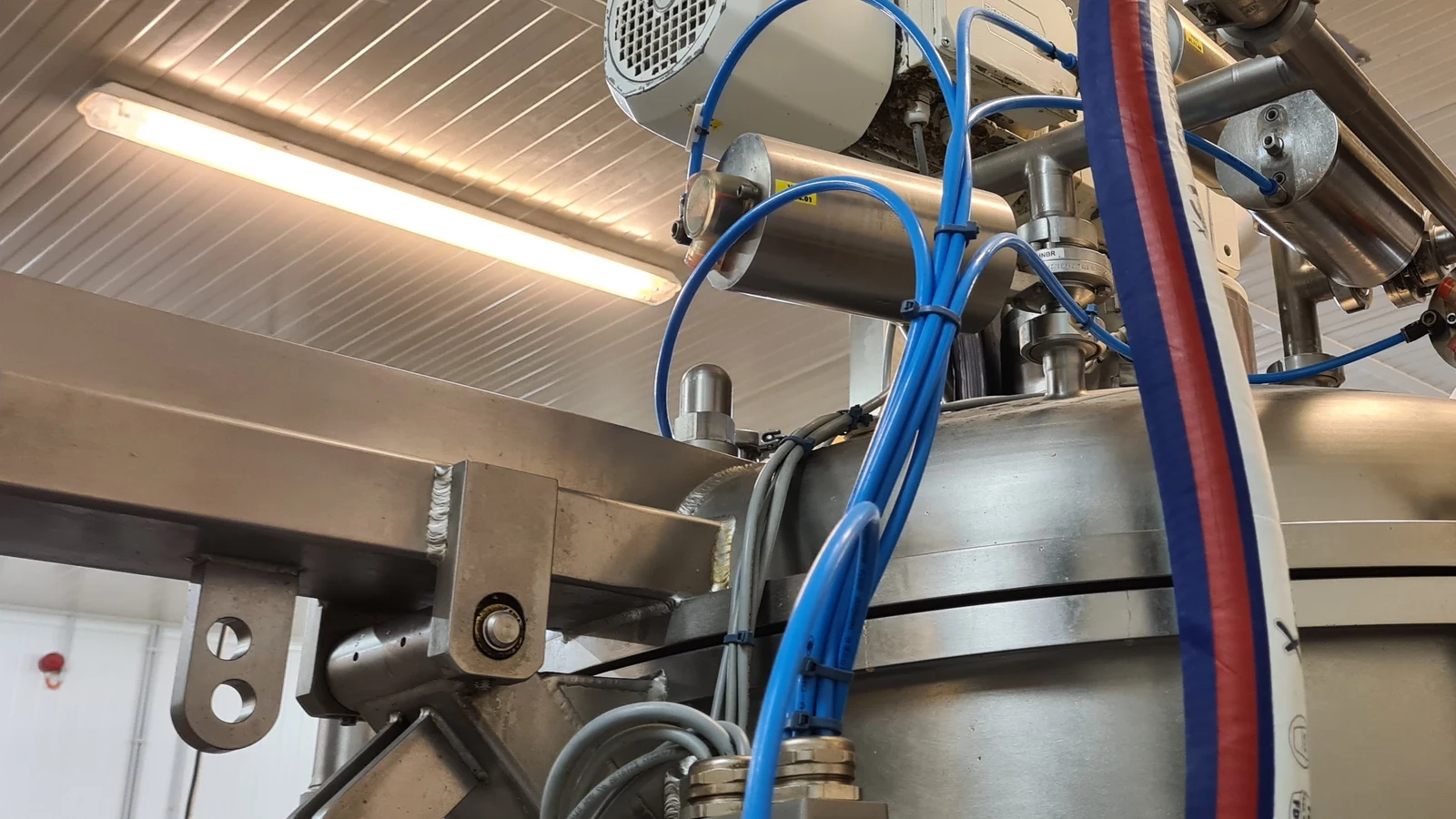 Cuve de process en inox dans un atelier agroalimentaire, avec son moteur d'agitation, ses flexibles et ses raccords instrumentés