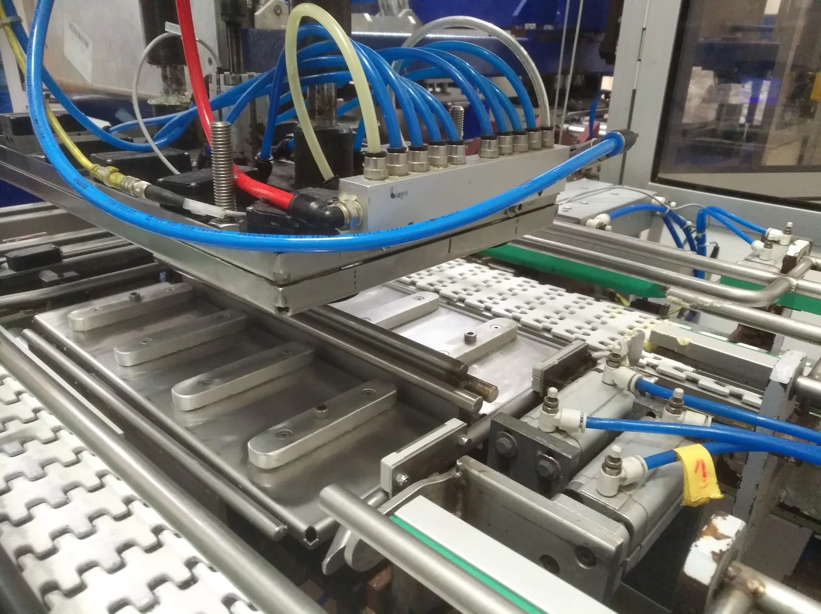 Distributeur pneumatique et vérins alimentés par des tubes bleus au-dessus du convoyeur d'une ligne de conditionnement
