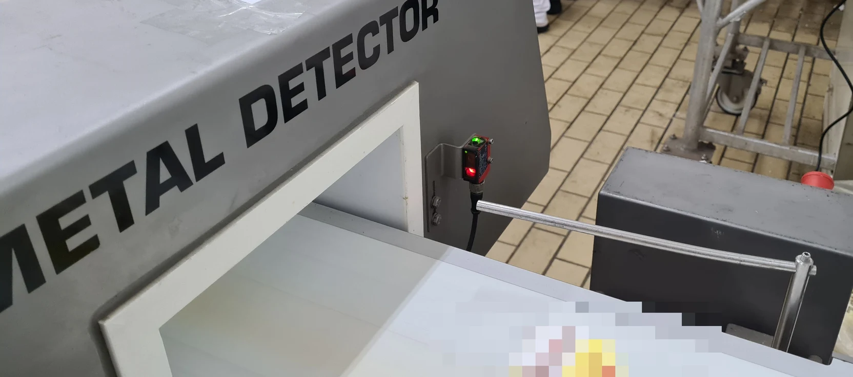 Cellule photoélectrique fixée sur le bâti d'un détecteur de métaux, au-dessus de la bande transporteuse d'une ligne de conditionnement