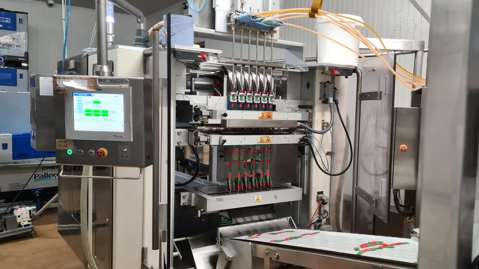 Machine d'ensachage multipistes dans un atelier de conditionnement, pupitre de commande à gauche et convoyeur de sortie au premier plan