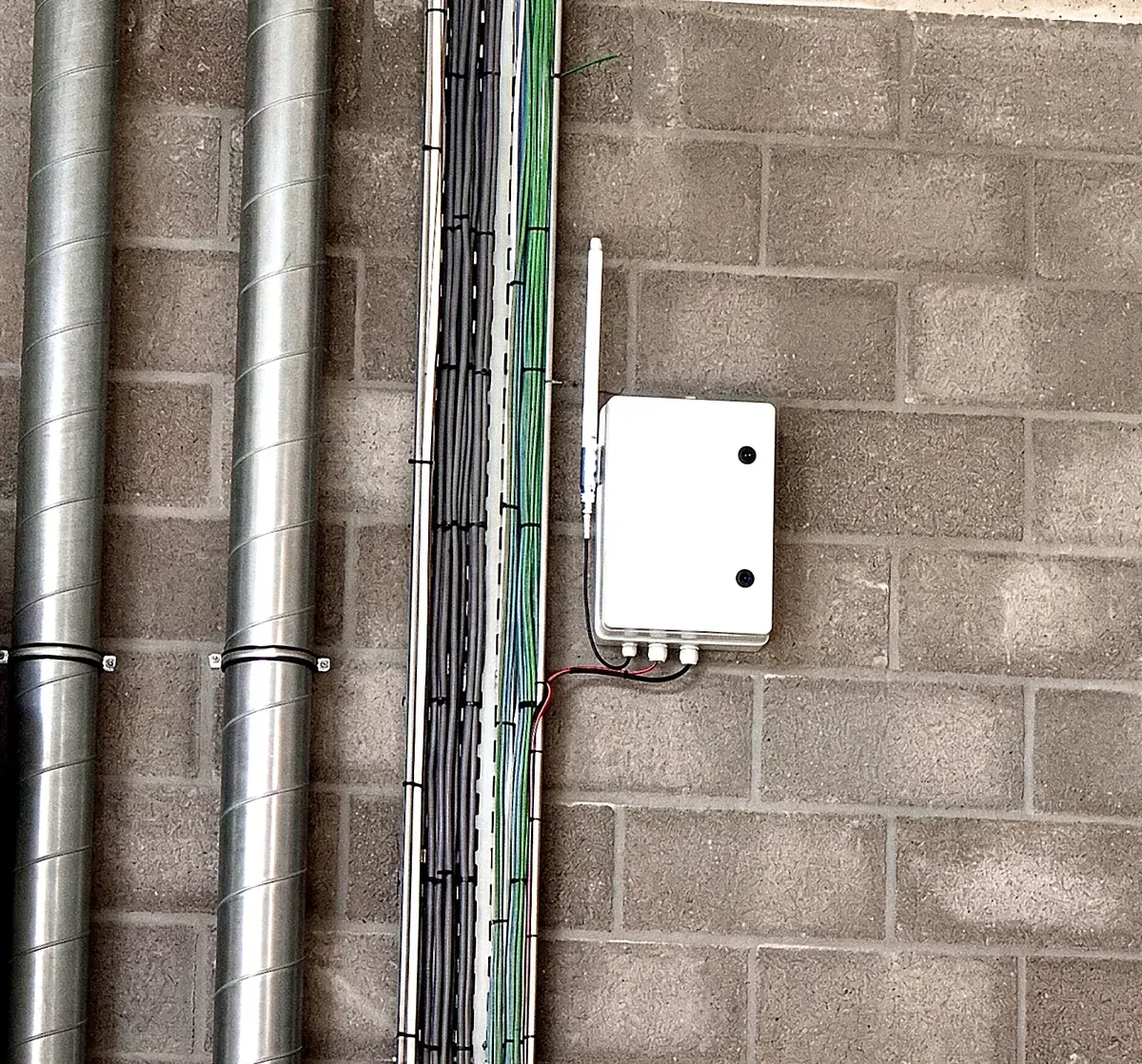 Gateway LoRaWAN fixée sur un mur en blocs de béton d'un atelier, antenne verticale, à côté d'un chemin de câbles et de gaines de ventilation.